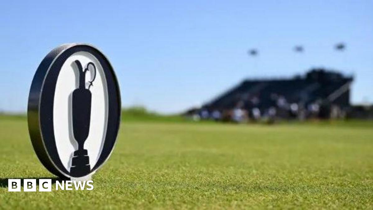 An Open logo coin on the course of Royal Portrush. A blurred bandstand can be seen in the background.