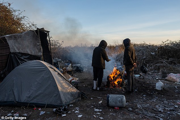 Iranian men, who did not wish to be identified, warm themselves by a fire in a migrant camp on January 20, 2024 in Loon-Plage, France