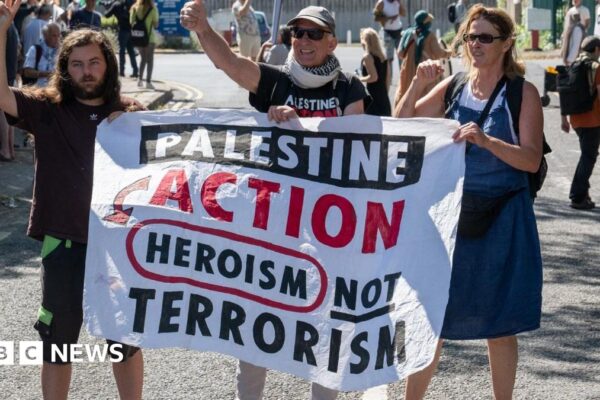 Three demonstrators hold a banner that reads "Palestine Action heroism not terrorism"