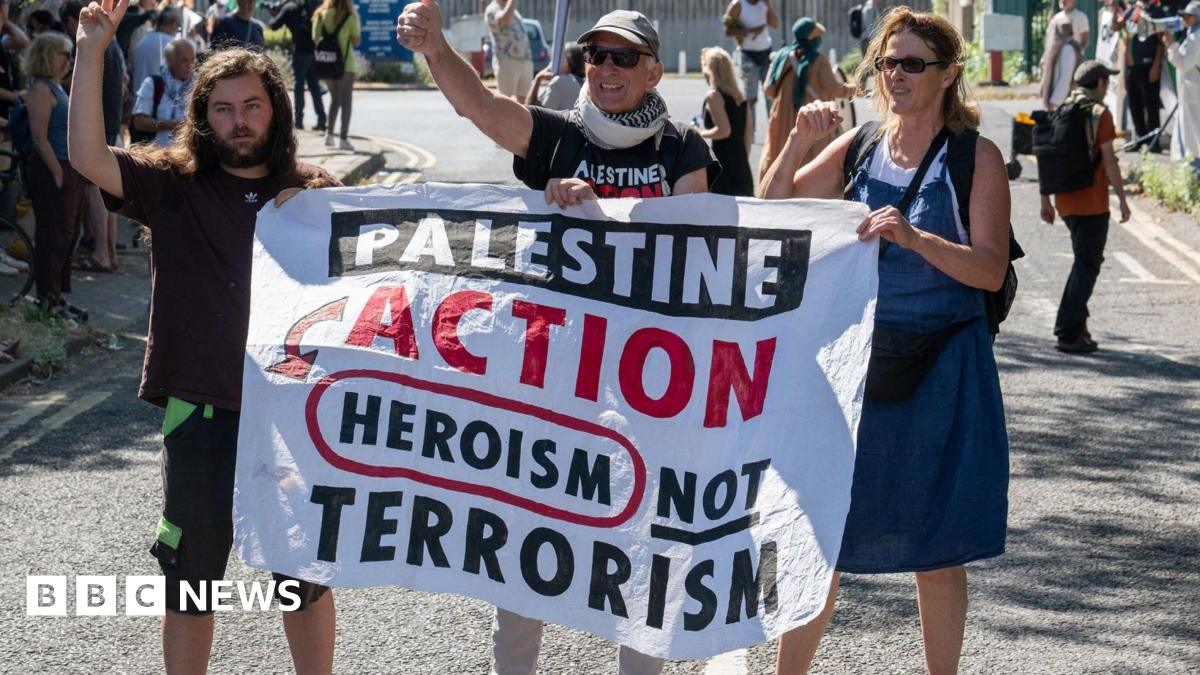 Three demonstrators hold a banner that reads "Palestine Action heroism not terrorism"