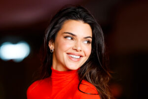 Kendall Jenner has long dark brown hair and wears a bright red turtle neck dress