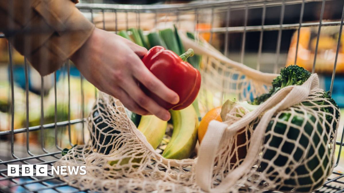 Close-up shot of female hand putting a red bell pepper into a mesh grocery bag.