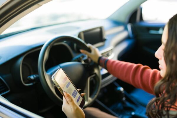 Teenager driving a car while holding and using a smartphone, representing distracted driving and road safety issues