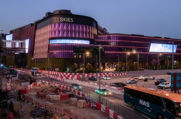 The 11 Skies retail and office complex near Hong Kong International Airport, featuring a modern design with illuminated signage and the surrounding area with ongoing construction work and barriers and vehicles on the road