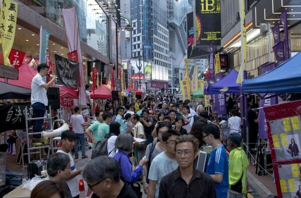 Crowd walking through a busy street market lined with colourful tents and banners