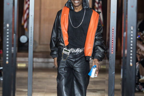 A$AP Rocky walking in a fashion show, wearing a black and orange outfit with a New York Yankees cap. Text overlay about Complex Style's Fashion Week.