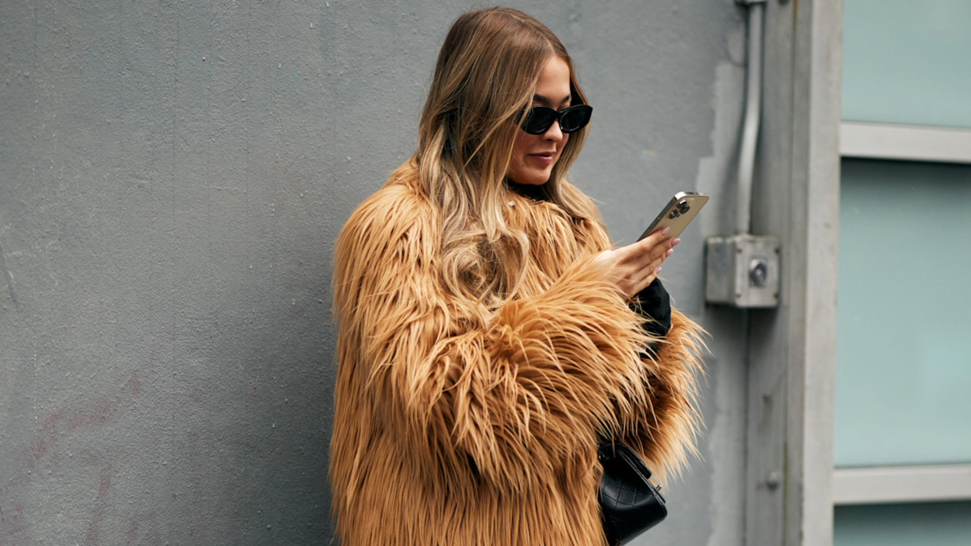 woman wearing a fur coat in New york with sunglasses and a phone.