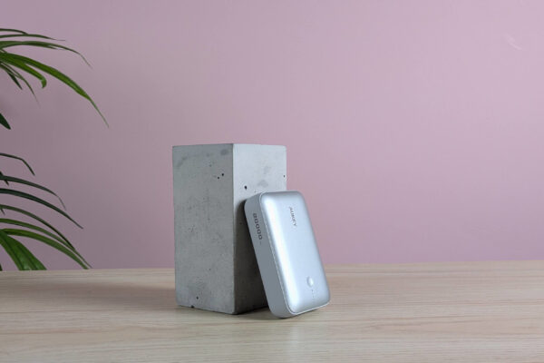 Aukey Spark Mini 20000 leaning on plinth on desk with pink wall and plant in background