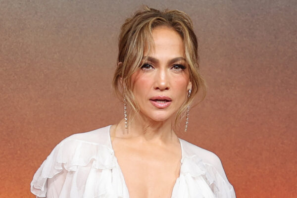 Jennifer Lopez wears a white tassled dress and stands in front of a sunset