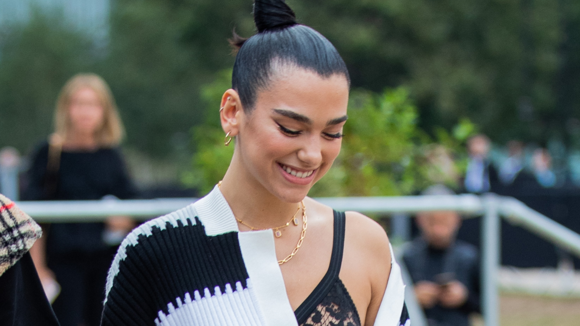 Dua Lipa has her hair in a high bun and wears an off-the-shoulder striped top with a lace bra underneath