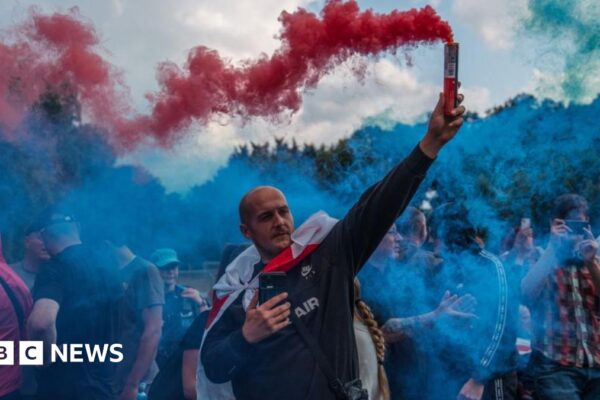 A man holds a flare during a protest outside The Bell Hotel on July 31, 2025 in Epping, England.