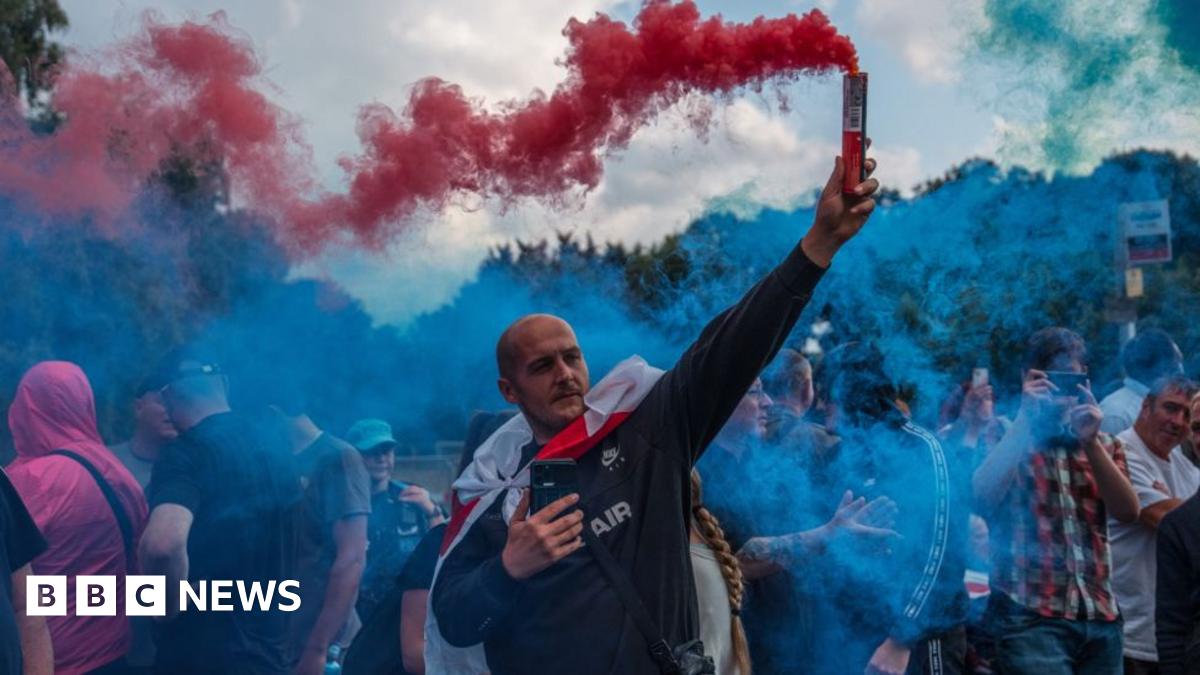 A man holds a flare during a protest outside The Bell Hotel on July 31, 2025 in Epping, England.