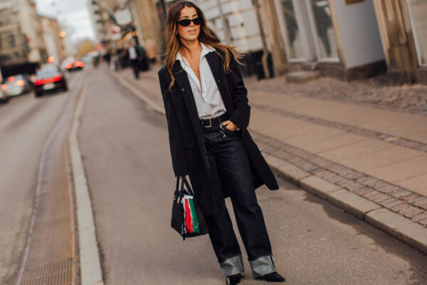 Fashion week attendee wearing sunglasses, button down shirt, black coat, cuffed jeans