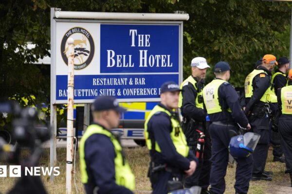 A group of police in high-vis vests stand outside a sign for The Bell Hotel in Epping.