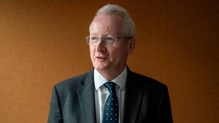 Niall Mackenzie, Acas chief executive, wearing a suit and patterned tie, stands against a plain brown background.