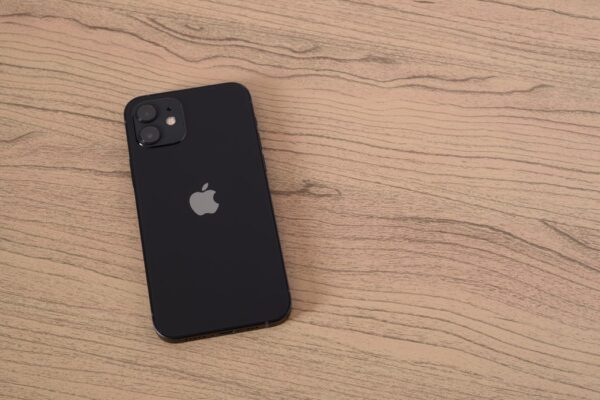 a black Apple iPhone sits face down on a light wood-grained table
