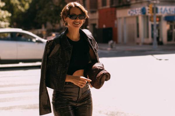 fashion week attendee wearing sunglasses and leather jacket over shoulders