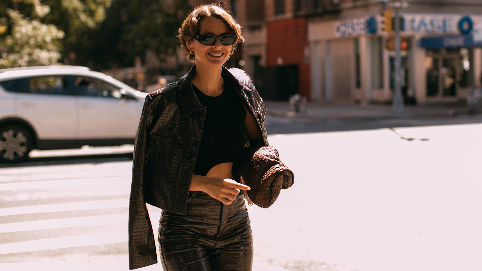 fashion week attendee wearing sunglasses and leather jacket over shoulders