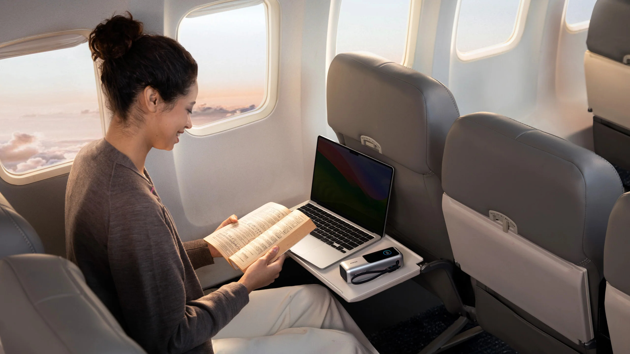 Anker power bank on aeroplane tray table with laptop and person reading a book