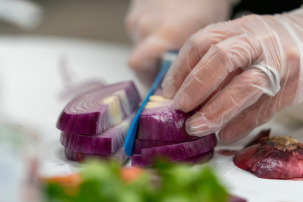 Closeup of hands with knife cutting a purple onion.