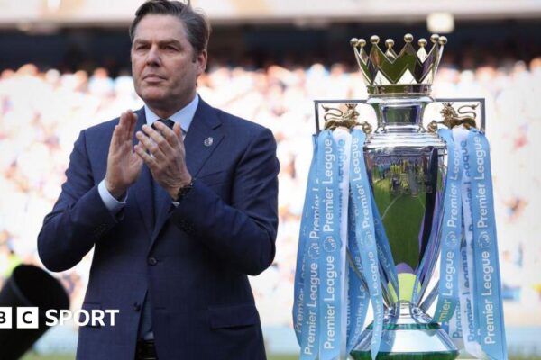 Richard Masters standing next to the Premier League trophy, which is in Manchester City colours