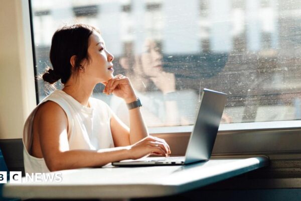 Young business woman looks out the train window while using her laptop on a table