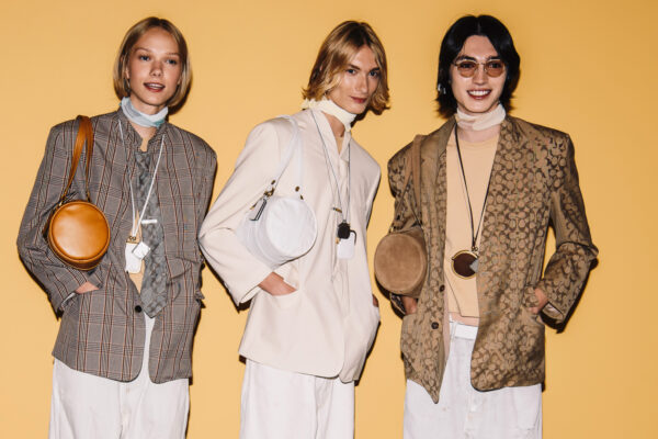 three models wearing the coach kisslock bag in front of a plain wall