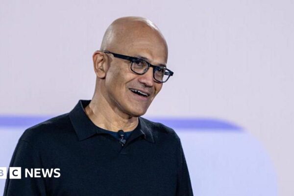 Satya Nadella smiling, wearing glasses and a black sweater