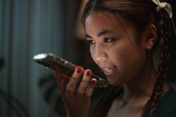 A young woman talks on a cellphone, her face illuminated by the glow of the phone screen.