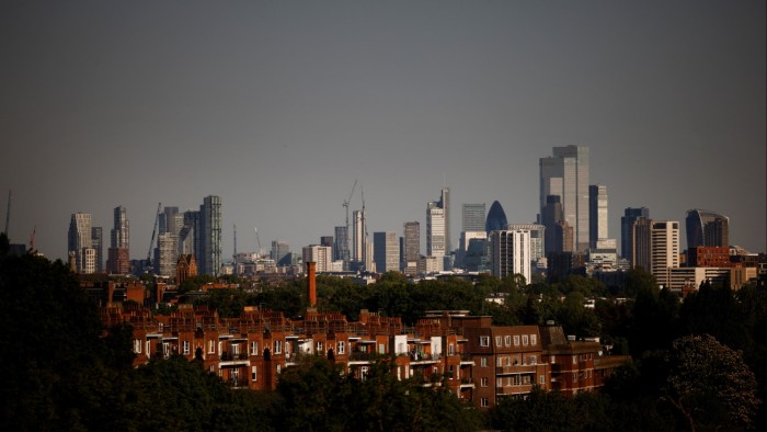 Panoramic view of the London skyline with modern skyscrapers and red-brick buildings in the foreground on a clear spring day.