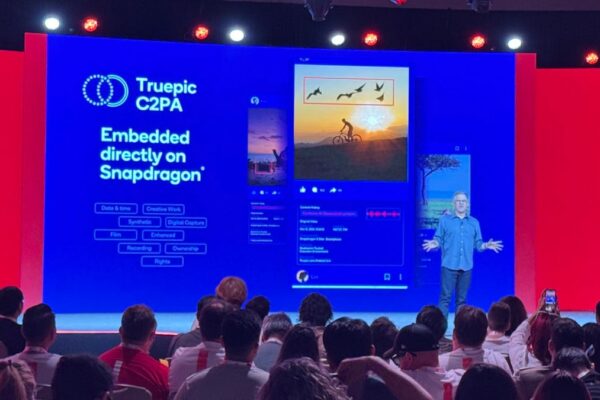 A man stands on stage with a presentation behind him announcing new phone features.