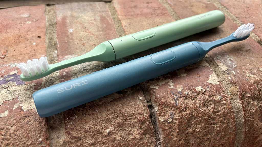Suri electric toothbrushes in green and blue, placed on a brick shelf