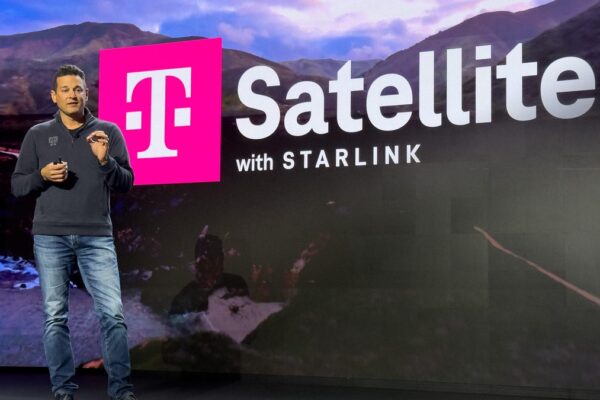 Man on stage speaking with a large screen behind him with information about the T-Satellite feature