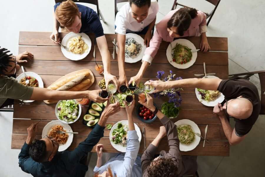 An aerial view of a table laden with vegan food and a group of people raising their glasses in a toast.