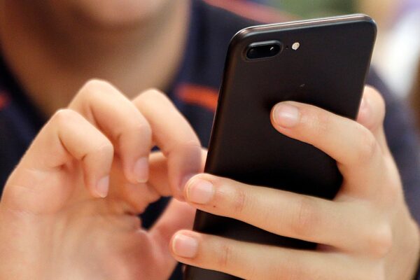 A person holds and uses a black smartphone with both hands, with their face partially out of frame.