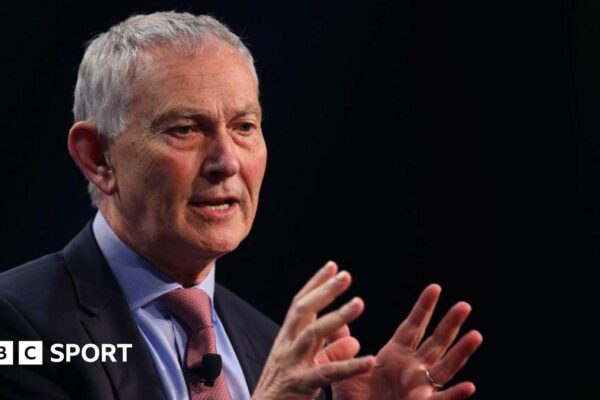 Richard Scudamore holding his hands open in front of him while giving a talk at a conference