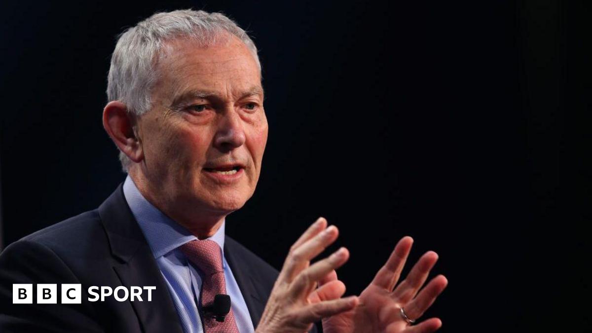 Richard Scudamore holding his hands open in front of him while giving a talk at a conference
