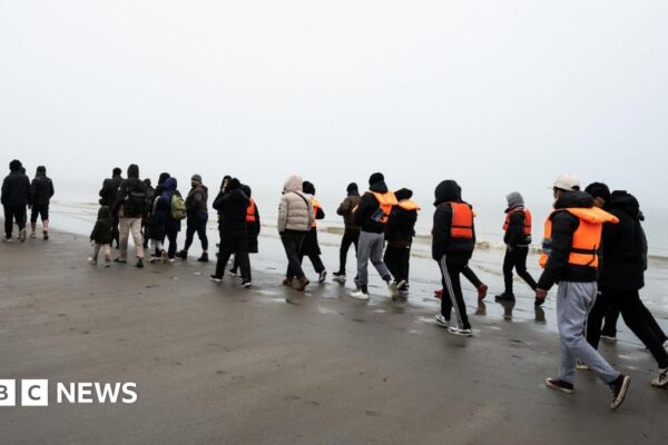 A group of migrants, some wearing lifejackets walk along a beach in France before taking a boat to the UK.