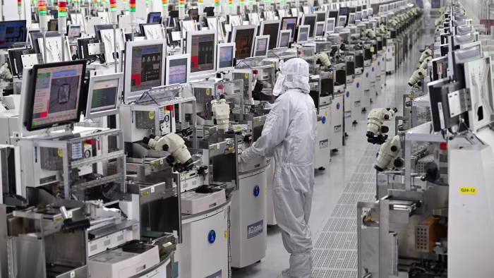 A technician in protective clothing operates equipment among rows of chip manufacturing machines at a semiconductor plant.
