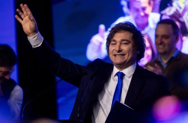 Javier Milei waves and smiles on stage after Argentina’s mid-term elections, with supporters clapping in the background.