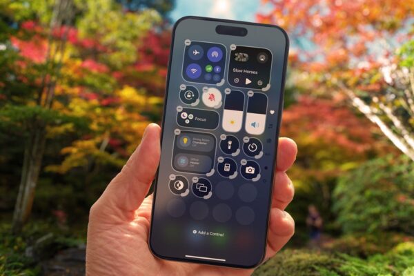 A hand holds an iPhone in front of a sandy beach and ocean scene..