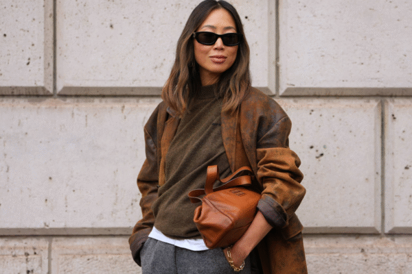 PARIS, FRANCE - OCTOBER 06: Aimee Song wears long wavy dark brown hair with center part, black rectangular sunglasses, small gold hoop earrings, a gold chain bracelet, a brown leather shoulder bag, a distressed brown suede oversized blazer jacket, an olive-green wool crewneck sweater, a white cotton T-shirt with visible hem, grey wool wide-leg trousers, outside Miu Miu, during Paris Fashion Week - Womenswear Spring Summer 2026, on October 06, 2025 in Paris, France (Photo by Edward Berthelot/Getty Images)