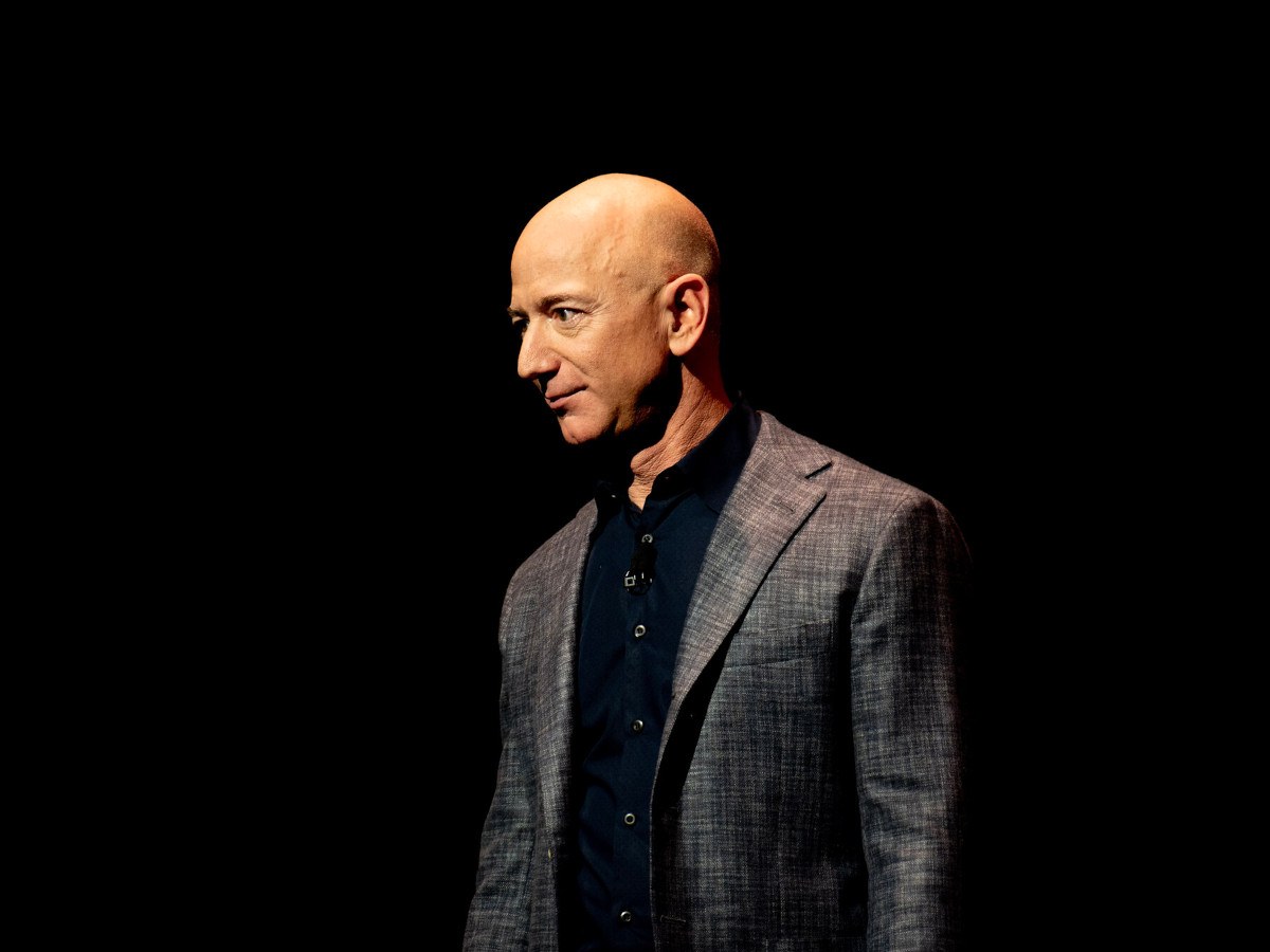 A bald man in a dark suit in a black background.