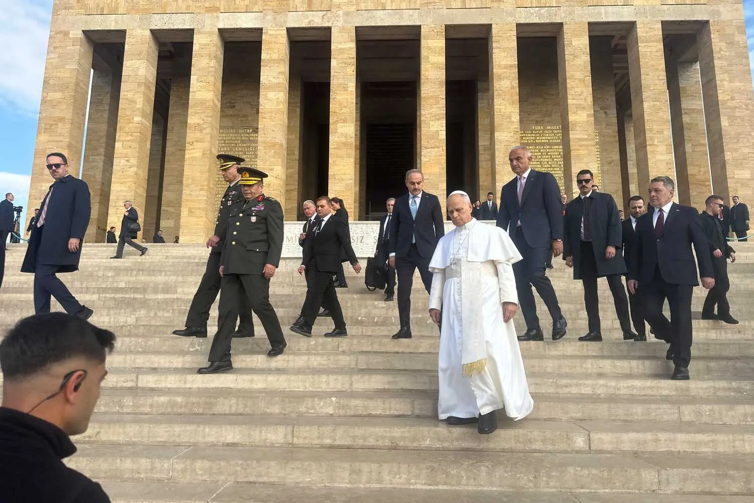 A group of people, including Pope Leo, walk down wide stone steps. A large stone building with tall columns stands in the background.