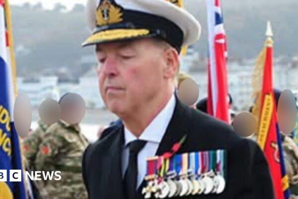 Close-up of the array of medals the man was wearing. He wears a black jacket, black tie and white shirt. A Remembrance Day poppy is pinned above the medals.