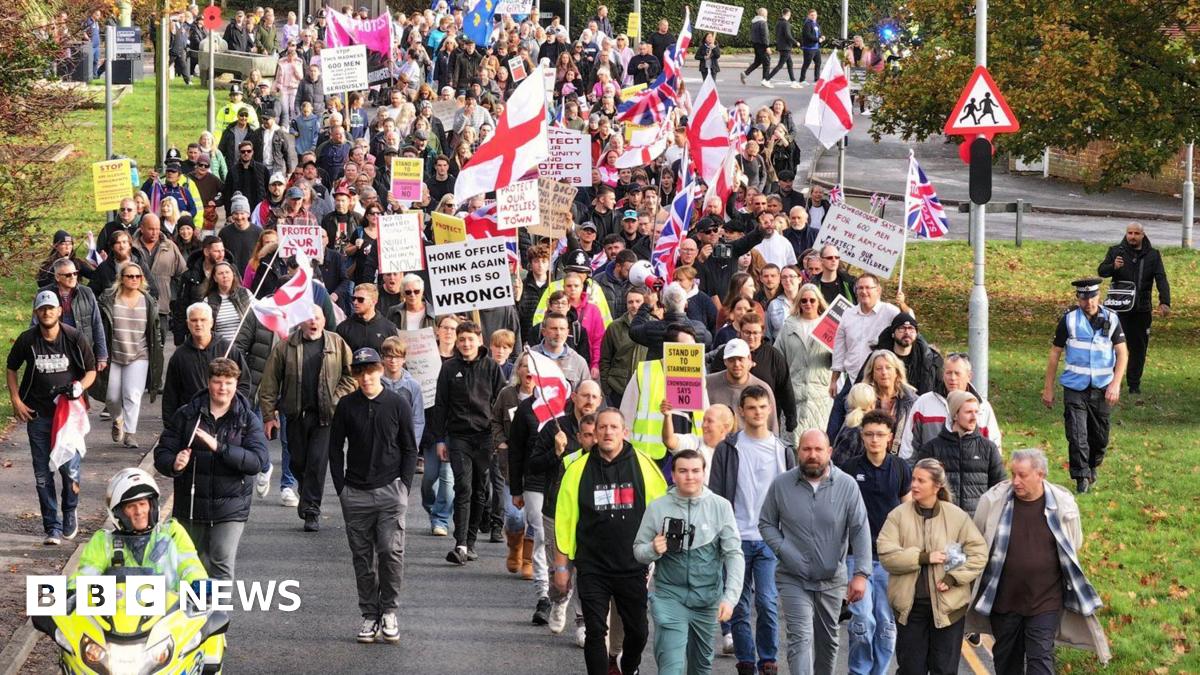 Hundreds of people holding St George flags marching along a residential road.