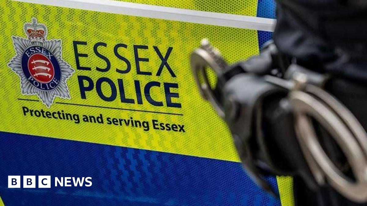 A green and blue Essex Police car with the hip of a police officer in front of it. That officer has a set of handcuffs on them.