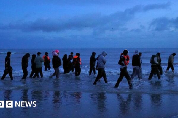 A group of migrants are seen at dawn wading through the shore in France to board a small boat