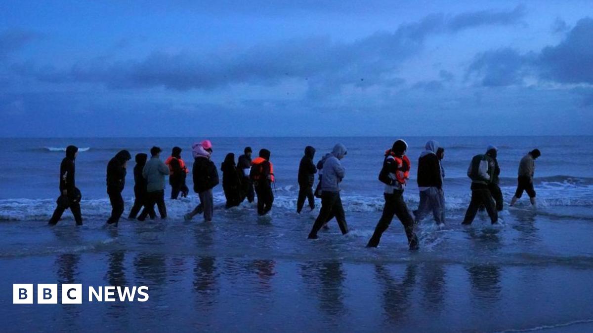 A group of migrants are seen at dawn wading through the shore in France to board a small boat