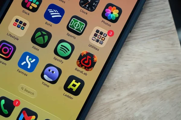 Smartphone screen showing various app icons including Slack, BofA, Xbox, Spotify, Instagram, and Gmail on a wooden surface.